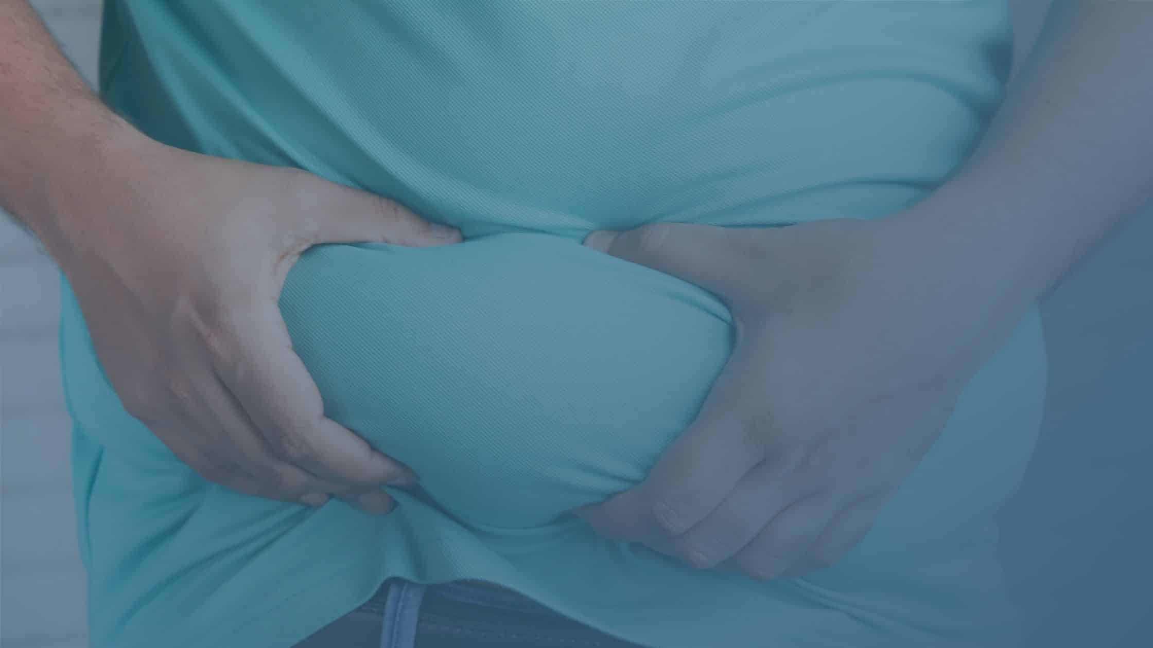 Pessoa apertando a região abdominal sobre a roupa, evidenciando excesso de gordura localizada.