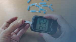 Pessoa utilizando um glicosímetro para medir os níveis de glicose no sangue, com tiras de teste ao fundo.